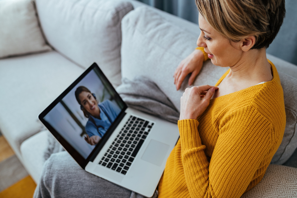 Young woman sitting on the sofa while talking with her doctor over a laptop.