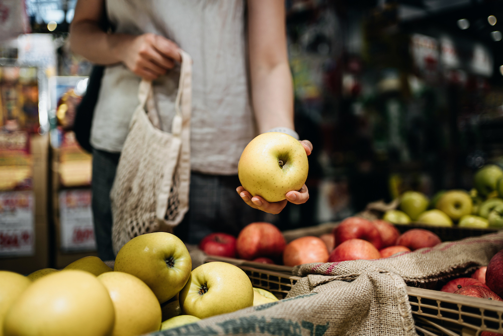 Close up of young person shopping for fresh organic fruits in farmer's market with a cotton mesh eco bag.