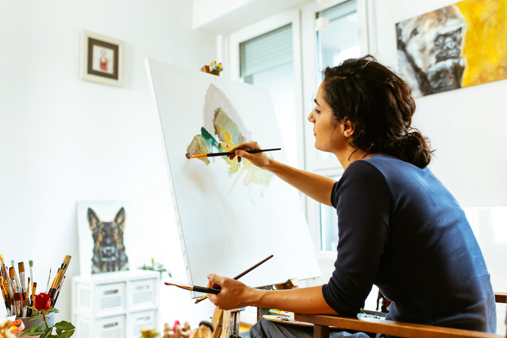 Beautiful female artist painting on a canvas with brush and palette in her studio