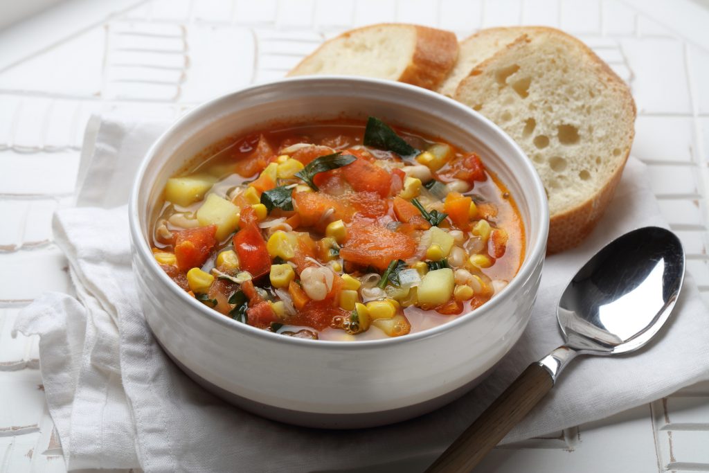 Seasonal vegetable soup with potatoes, carrots, onions, garlic, white beans, corn, tomatoes and parsley