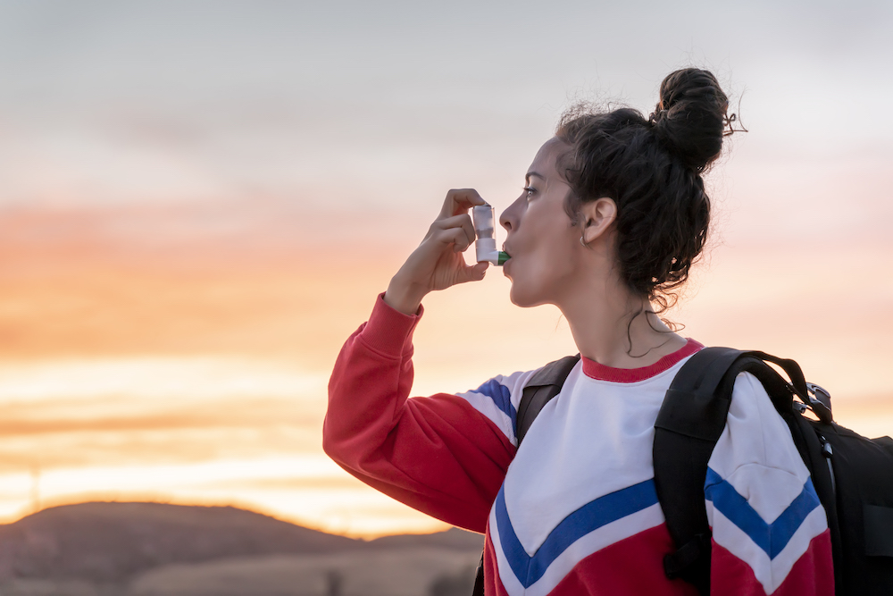 Millennial woman takes a break from her day hike in the lake to use her asthma inhaler