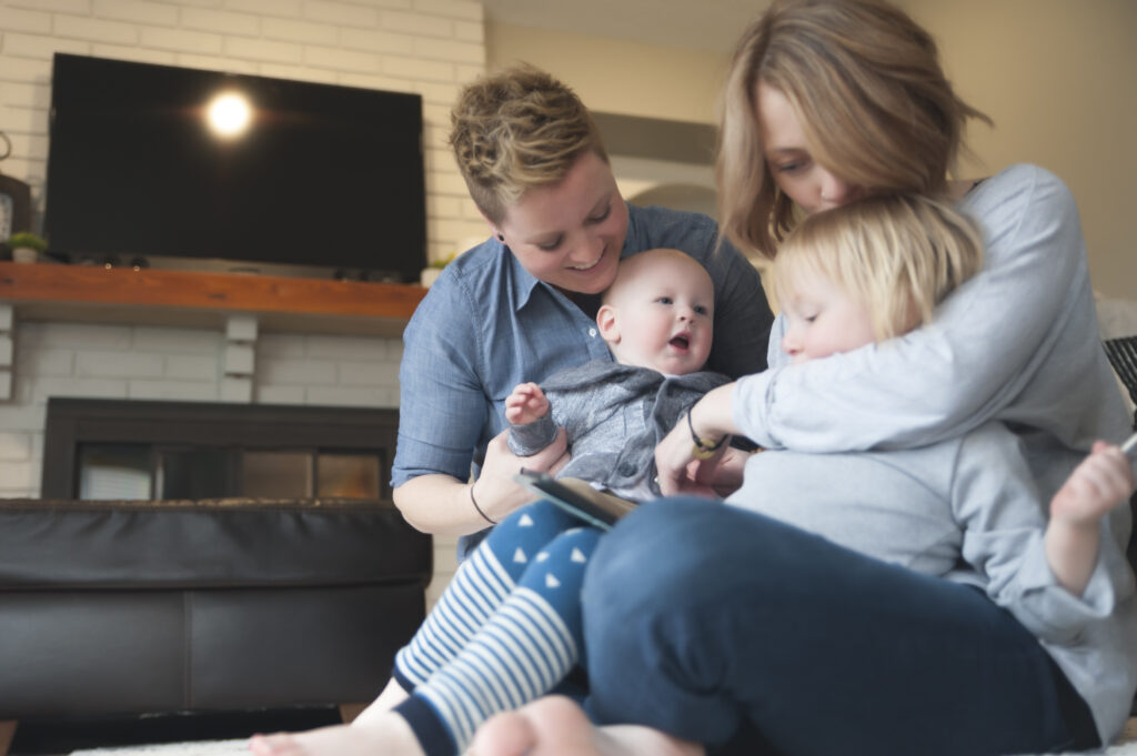 Two mothers parenting a one year old and 3 year old play in their suburban home indoors in Iowa